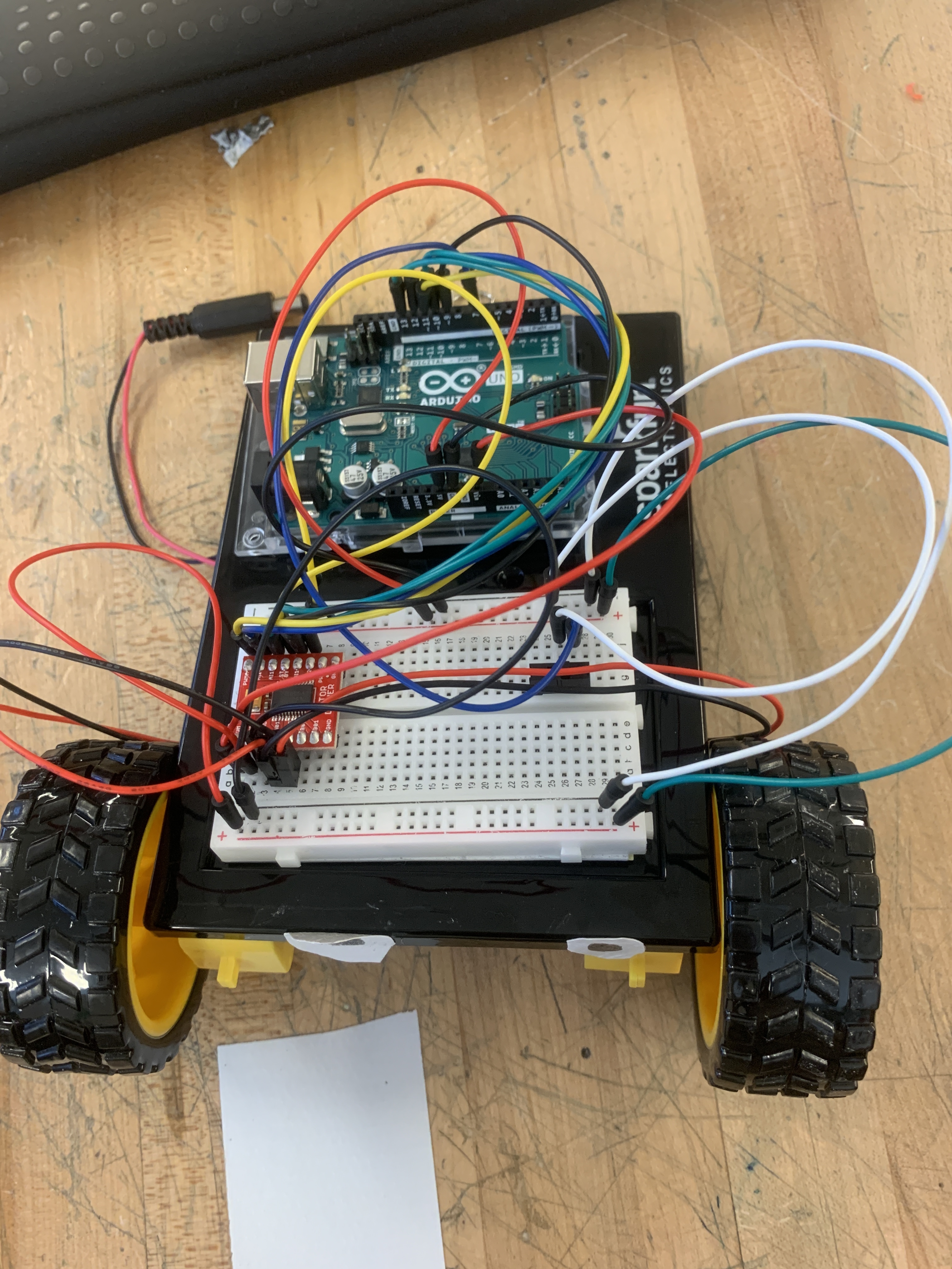 A mini arduino car with many colorful wires and a breadboard.