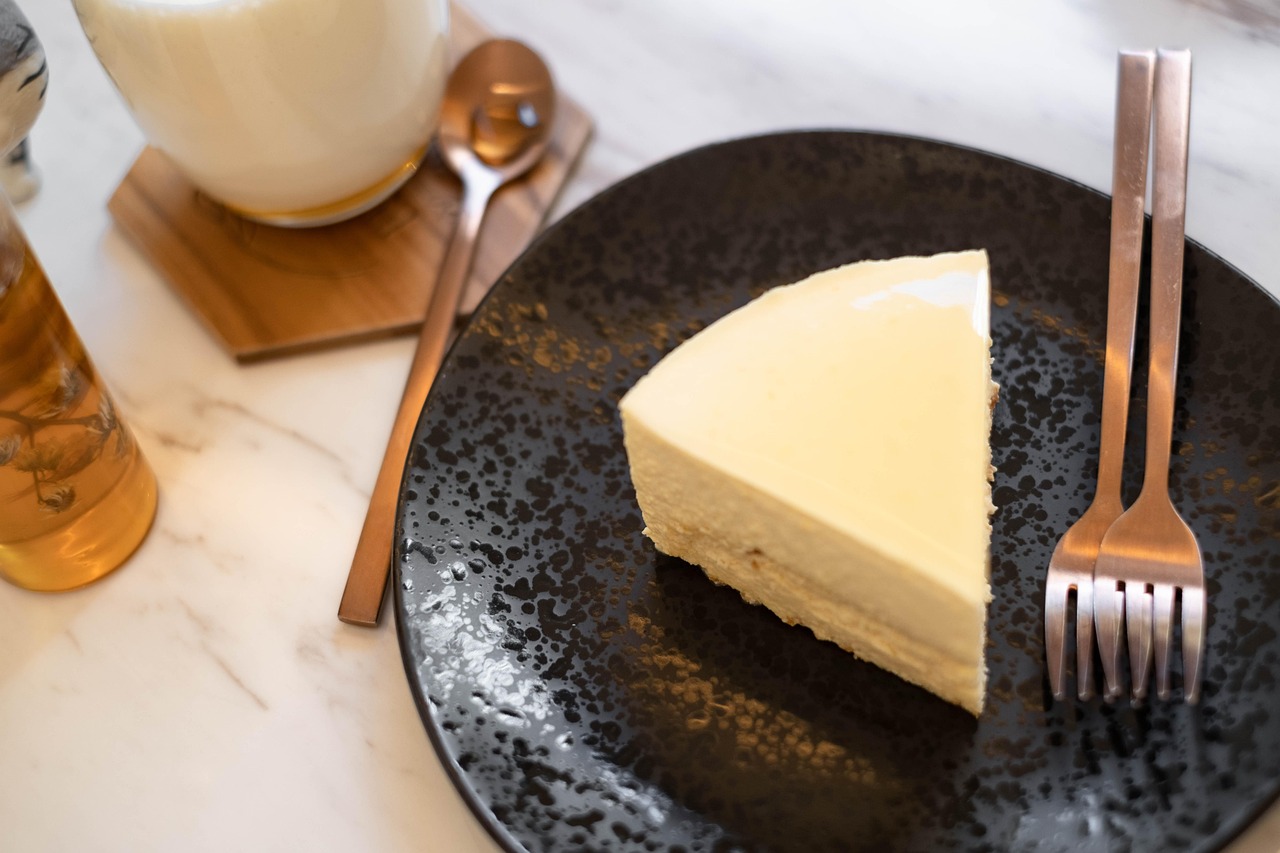 A slice of cheesecake on a black plate with forks.